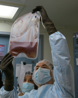 Photo: Two technicians in Penn Medicine's Clinical Cell and Vaccine Production Facility hold up a bag of modified T cells genetically edited to resist HIV infection.
