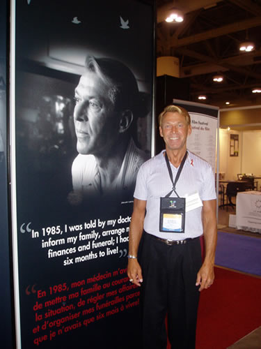 AIDS 2006 XVI International AIDS Conference: Bradford McIntyre standing beside his portrait at the Canada Booth - Leading Together: Canada Takes Action on HIV/AIDS. Poster caption - In 1985, 
I was told by my doctor to arrange my finances and funeral; I had six months to live.