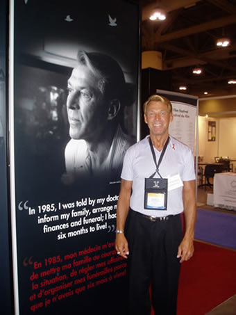 Bradford McIntyre, living with HIV since 1984, standing beside the 8 ft. poster portrait of himself, at the Canada Booth – Leading Together: Canada Takes Action on HIV/AIDS - XVI International AIDS Conference - August 13-18, 2006.