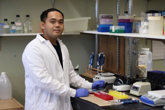 Erwin Taguiam, wearing a white lab coat, holds  small test tube in a lab