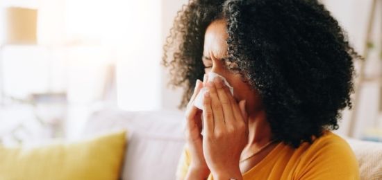 Person on a couch blowing nose with a tissue in a bright living room