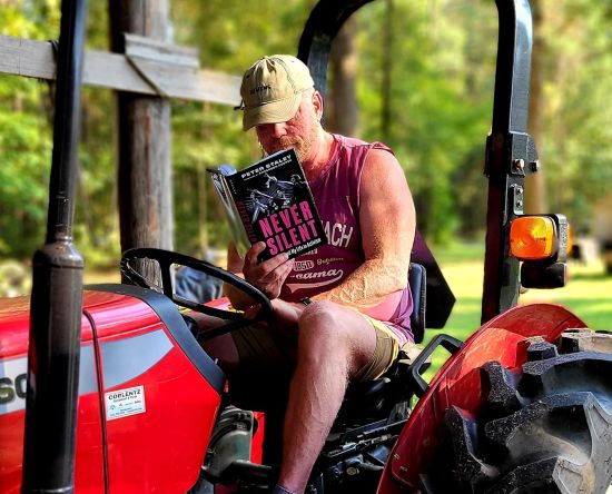 Mark S King reading Never Silent by Peter Staley on a tractor