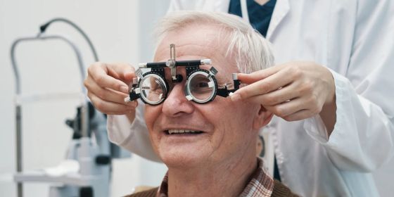 An older adult male patient smiles while getting an eye exam.